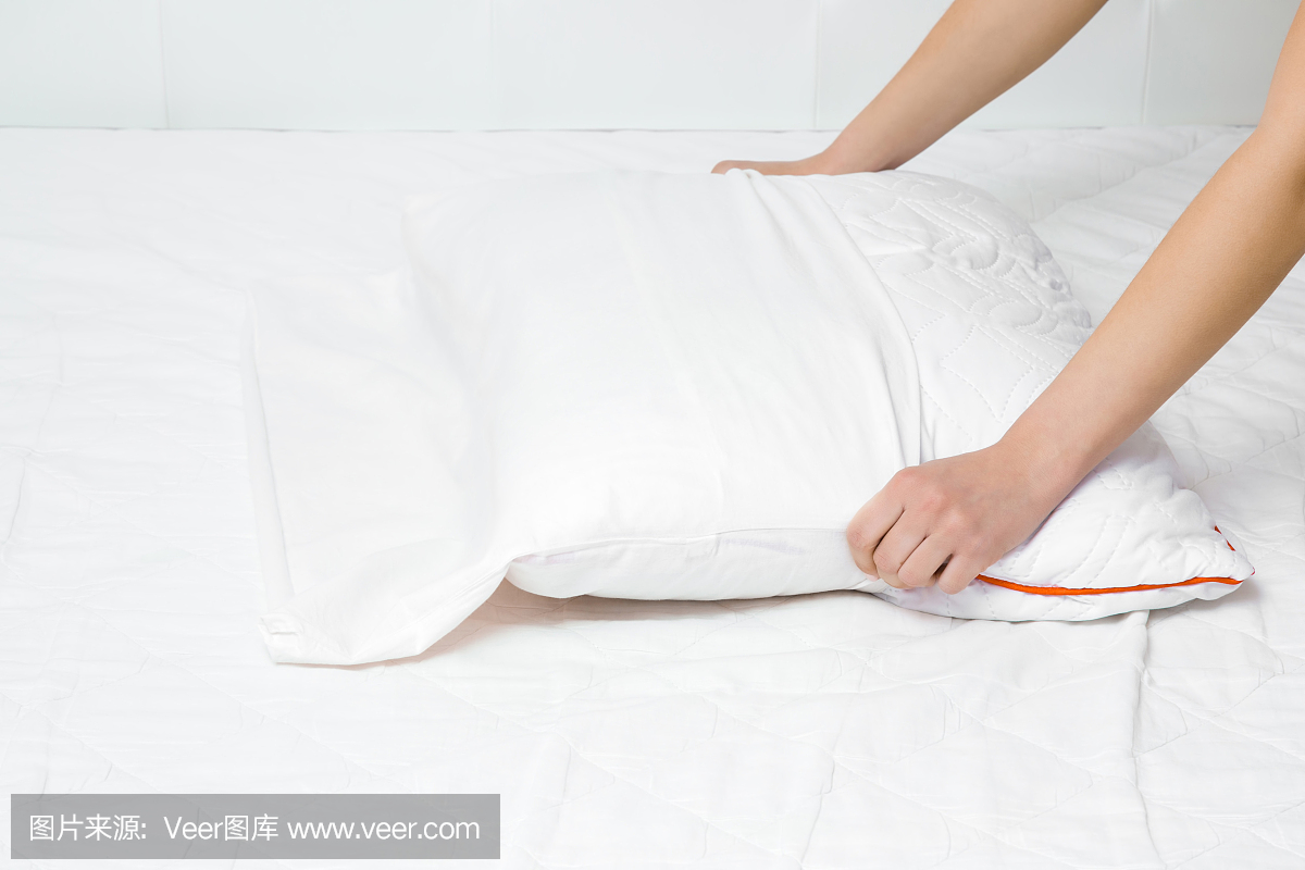 女人的双手在床垫表面更换枕头上的白色棉套。定期更换床上用品。特写镜头。